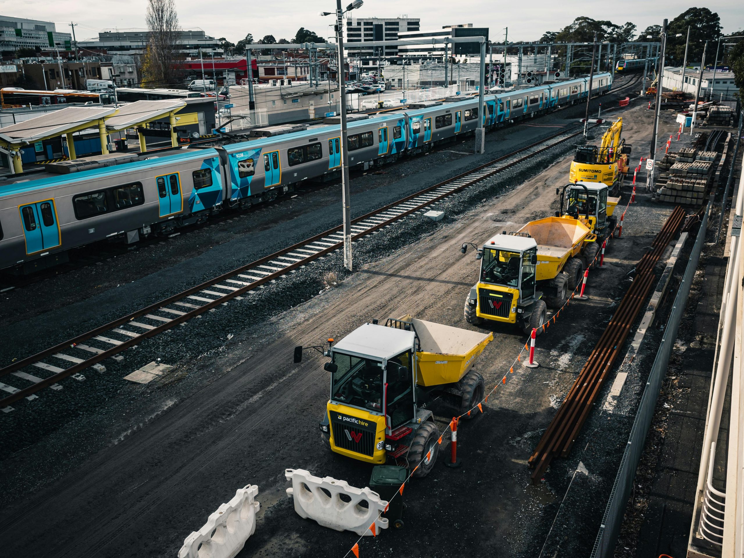 Construction vehicles working on a railway site next to a commuter train station.