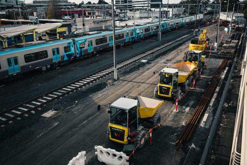 Construction vehicles working on a railway site next to a commuter train station.