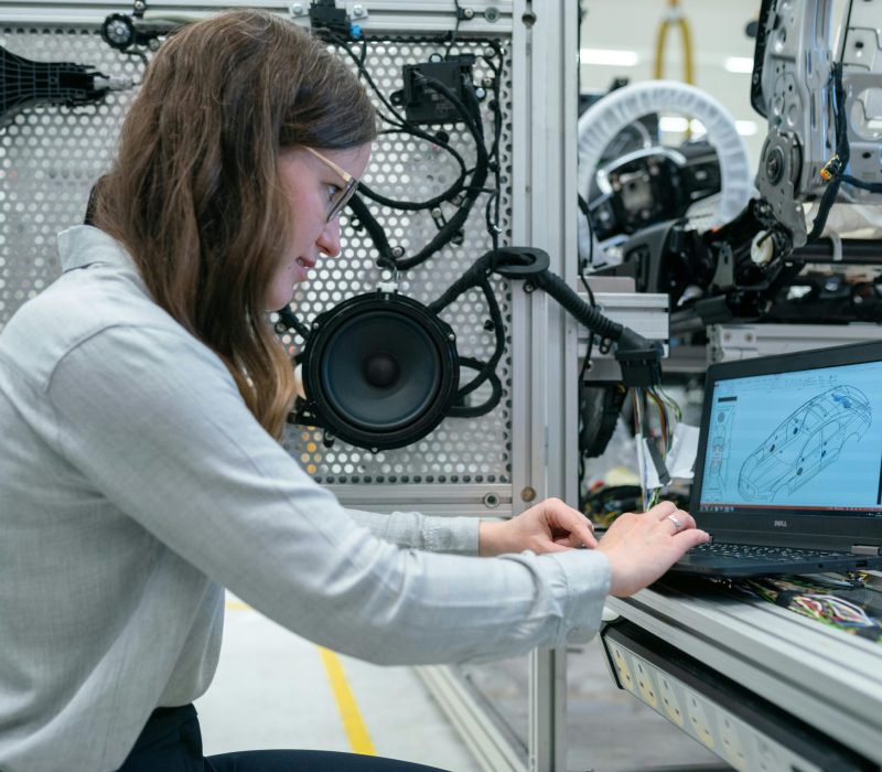 Woman conducting engineering research in a sound system workshop using a laptop.